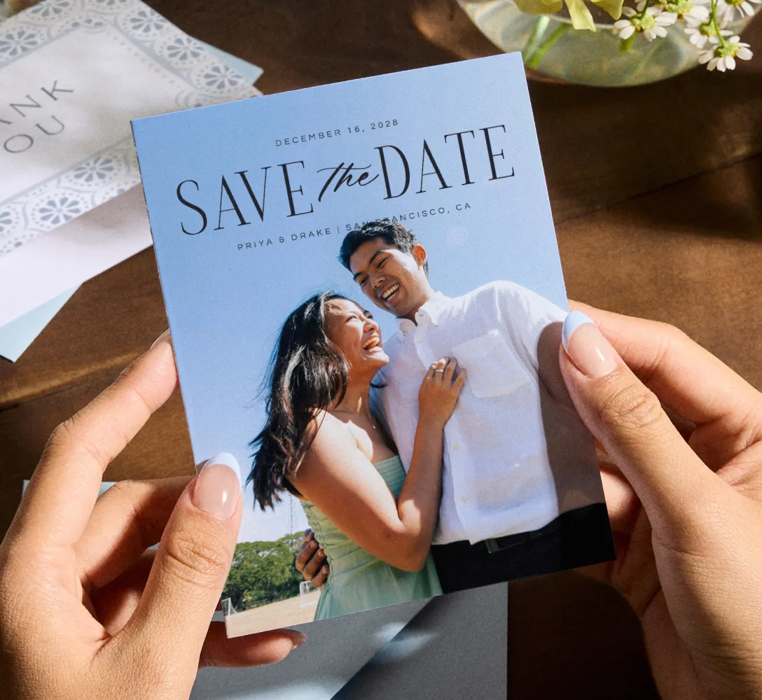 Hands holding a save the date card with a photo of a couple