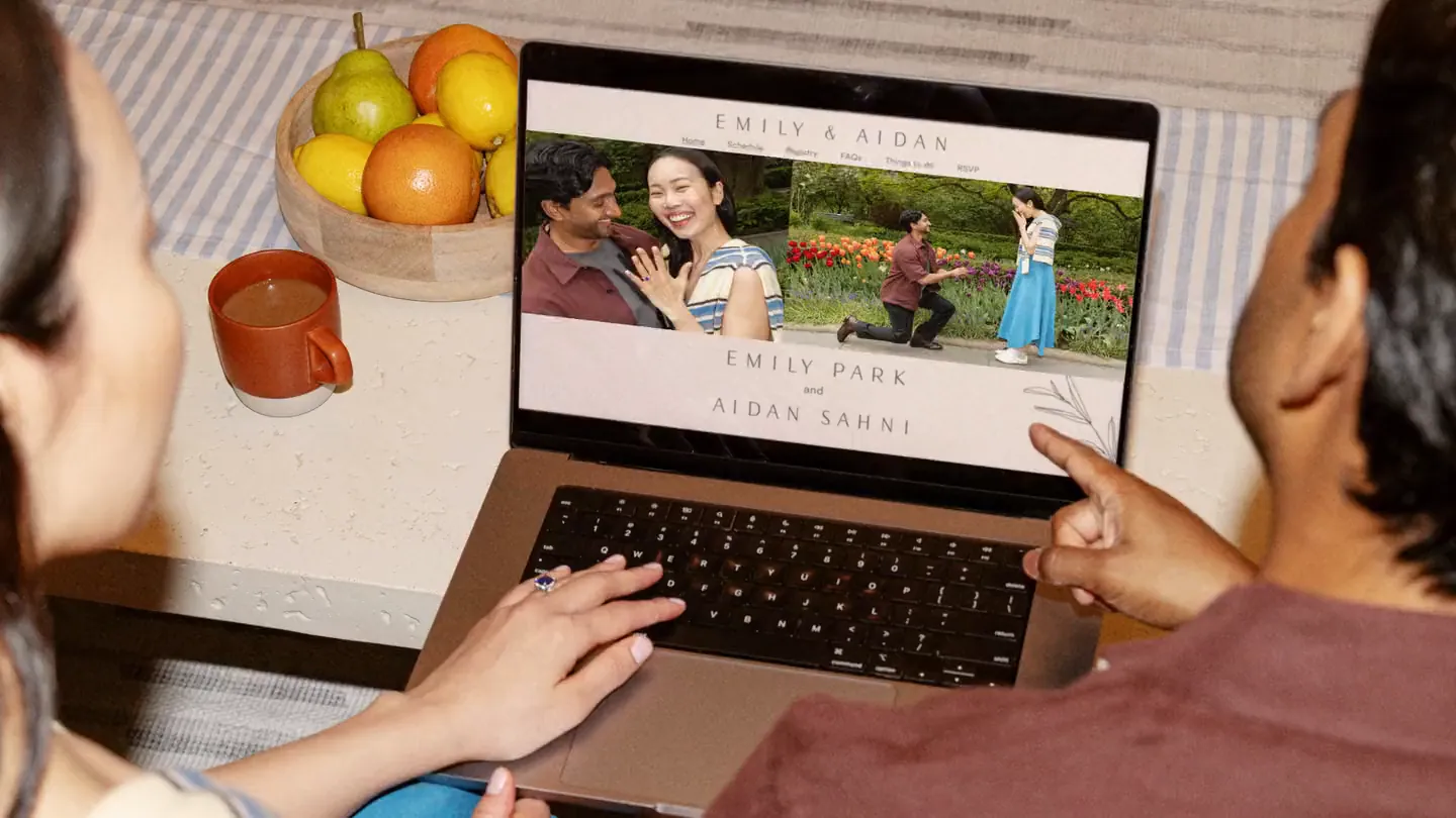 Couple watching a rotating photo carousel on their Zola wedding website on a laptop