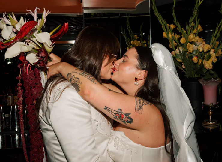 Couple sharing a kiss at their wedding, surrounded by floral arrangements with red and white flowers and yellow roses