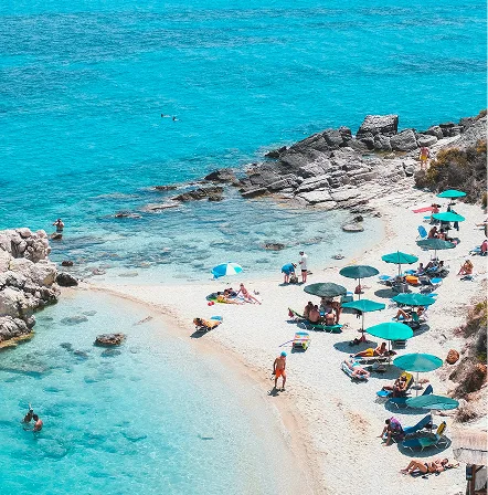 Sunbathers and striped umbrellas on a small beach beside a turquoise bay
