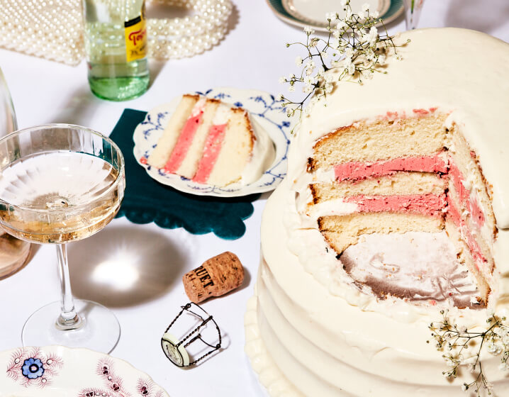 A white frosted wedding cake with a slice cut out next to a glass of champagne