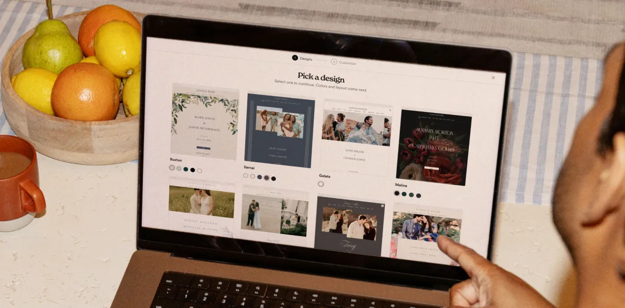 A laptop showing Zola's pick-a-design screen with wedding website templates
