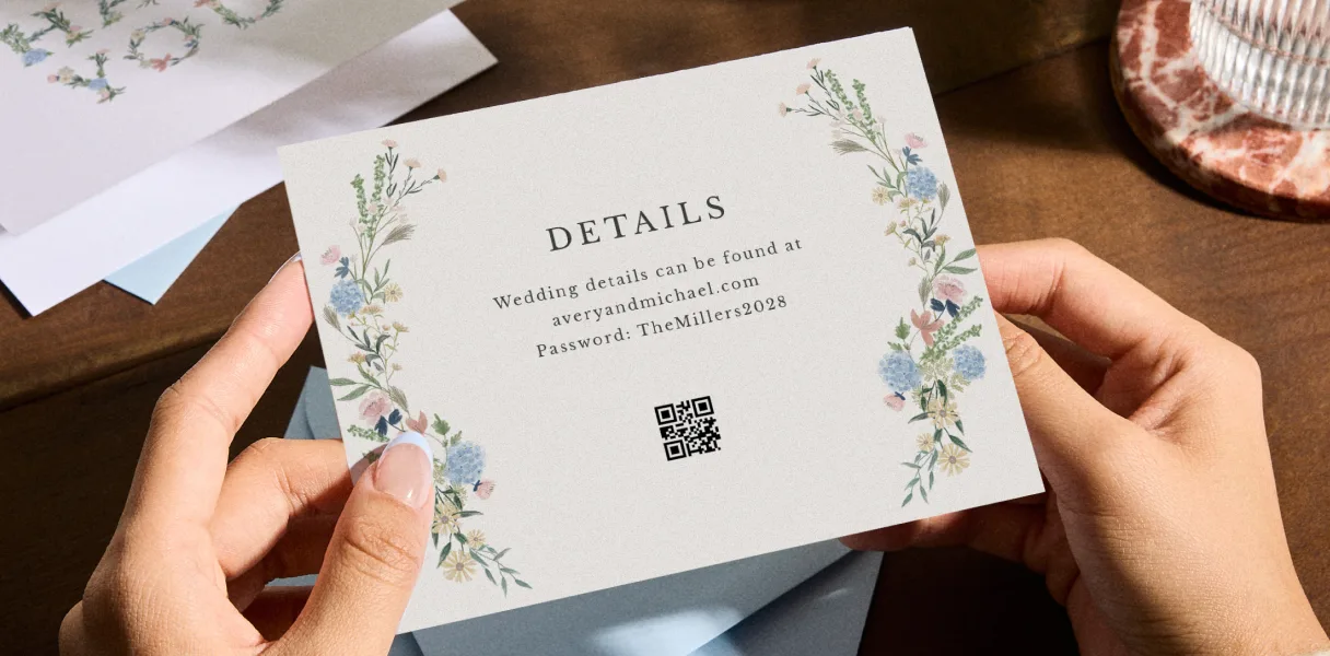 Hands holding a Zola wedding details card with a QR code and website URL